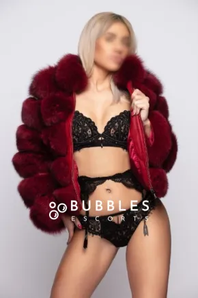 Robin standing in a furry puffer jacket and black lingerie 
