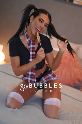 Roberta kneeling on the bed while licking a lollypop 